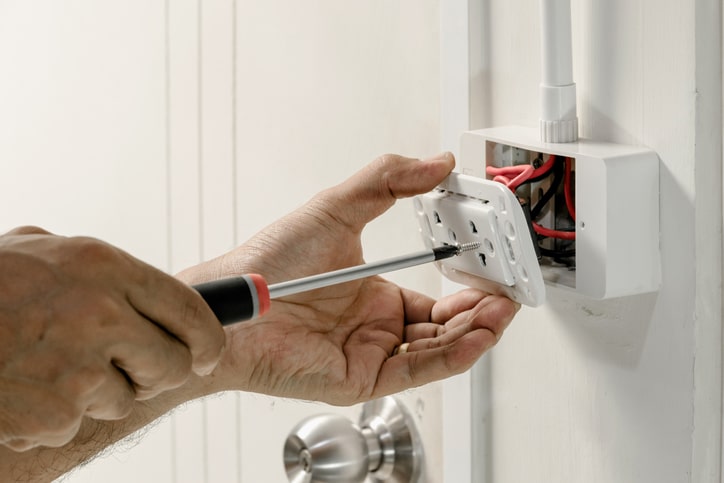 Electrician installing or repairing a wall outlet using a screwdriver and exposed wiring.